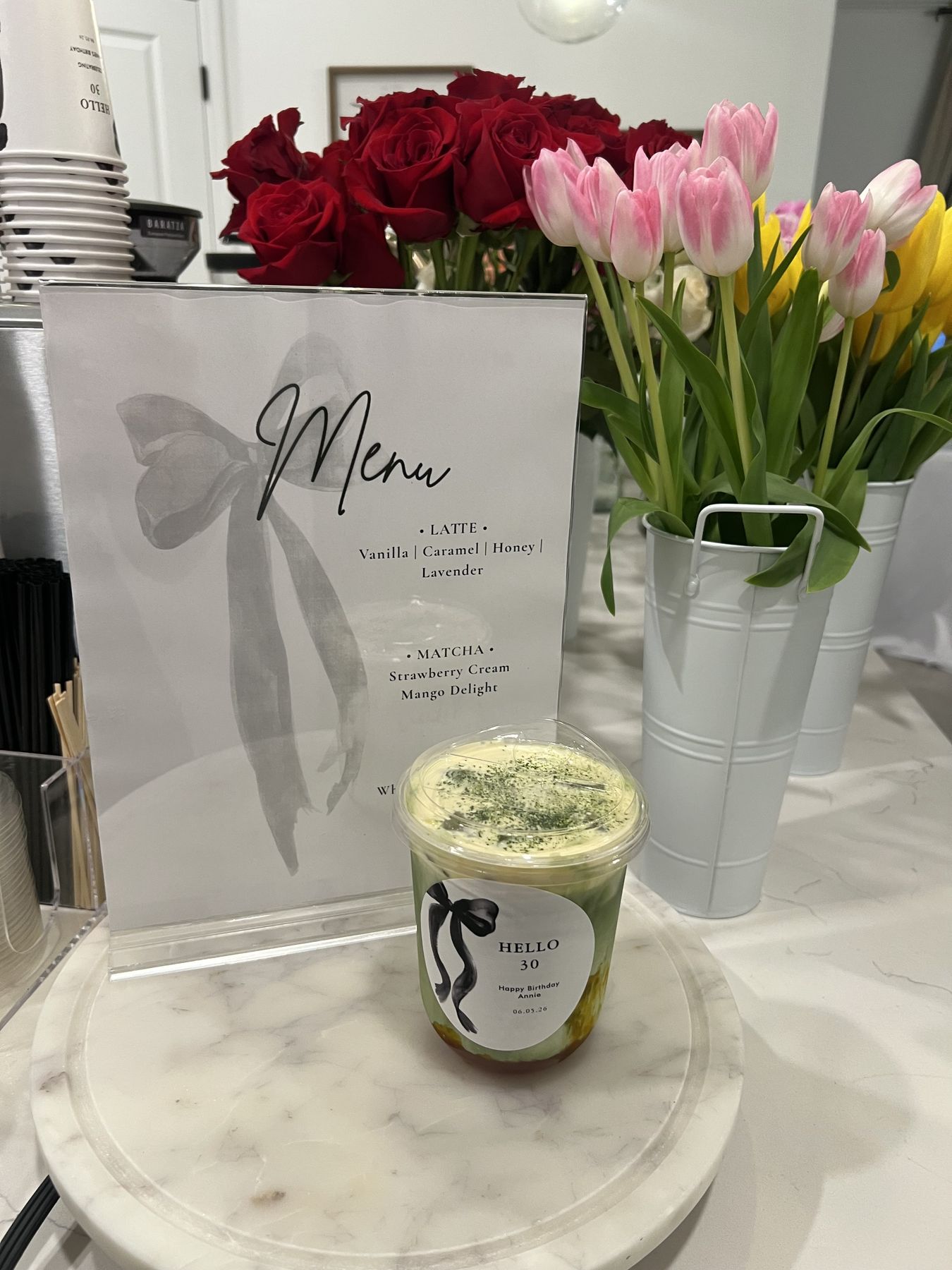 Iced matcha in front of a custom drink menu and tulips